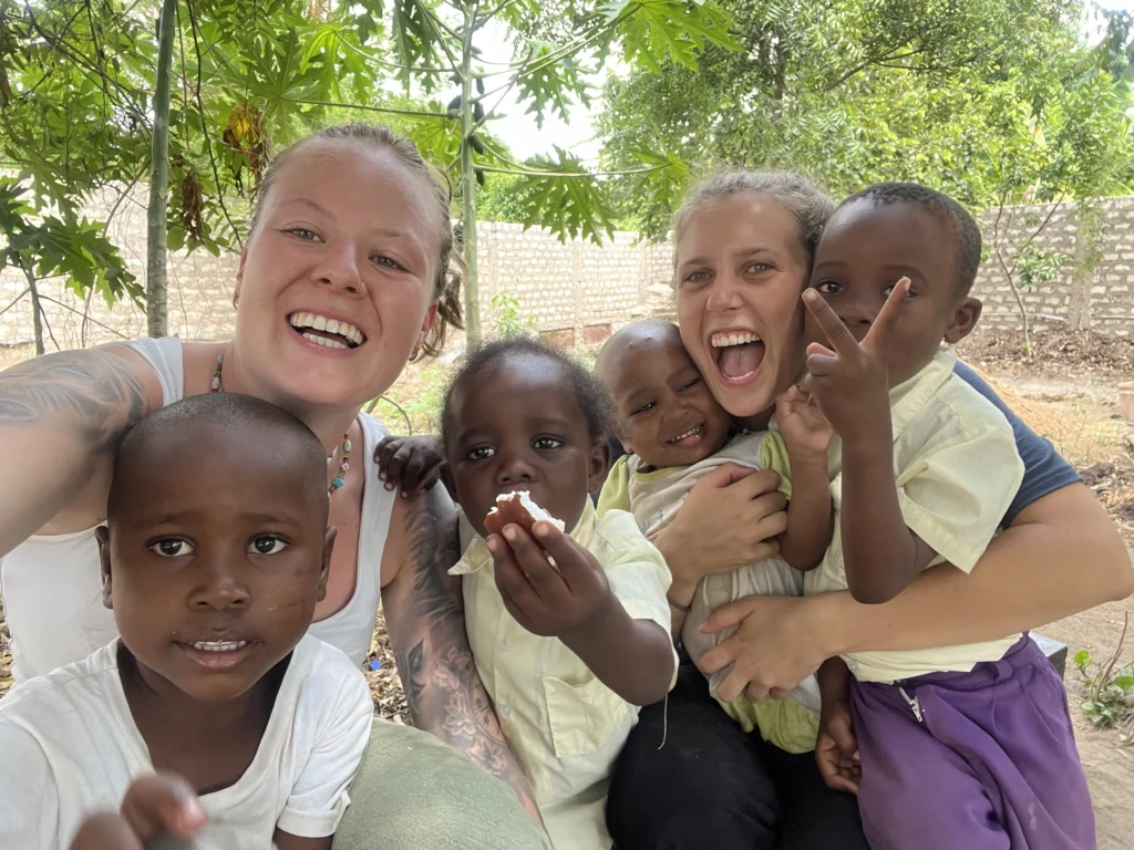 Zwei Supernurse-Pflegekräfte machen ein fröhliches Selfie mit vier lachenden afrikanischen Kindern – ein Moment der Freude und Verbundenheit.